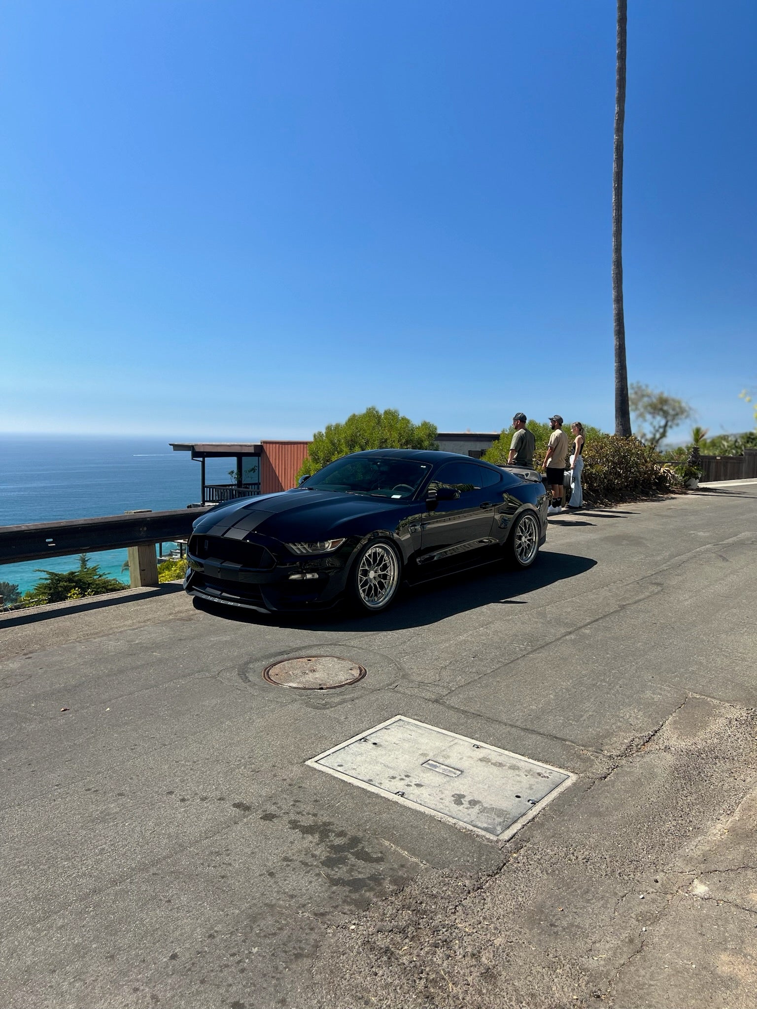 Black car parked on a road with ocean and blue sky in the background